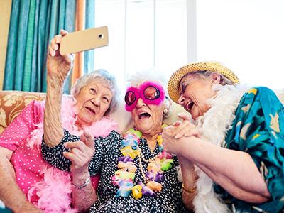 Drei ältere Frauen, Seniorinnen, bunt gekleidet, schauen sich lachend gemeinsam ein Smartphone an.