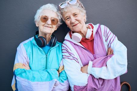 Zwei zufriedene ältere homosexuelle Frauen, Seniorinnen in bunter Sportbekleidung mit Kopfhörern