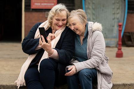 Zwei glückliche Seniorinnen schauen auf ein Smartphone und freuen sich über ihr gesundes Wohlergehen.